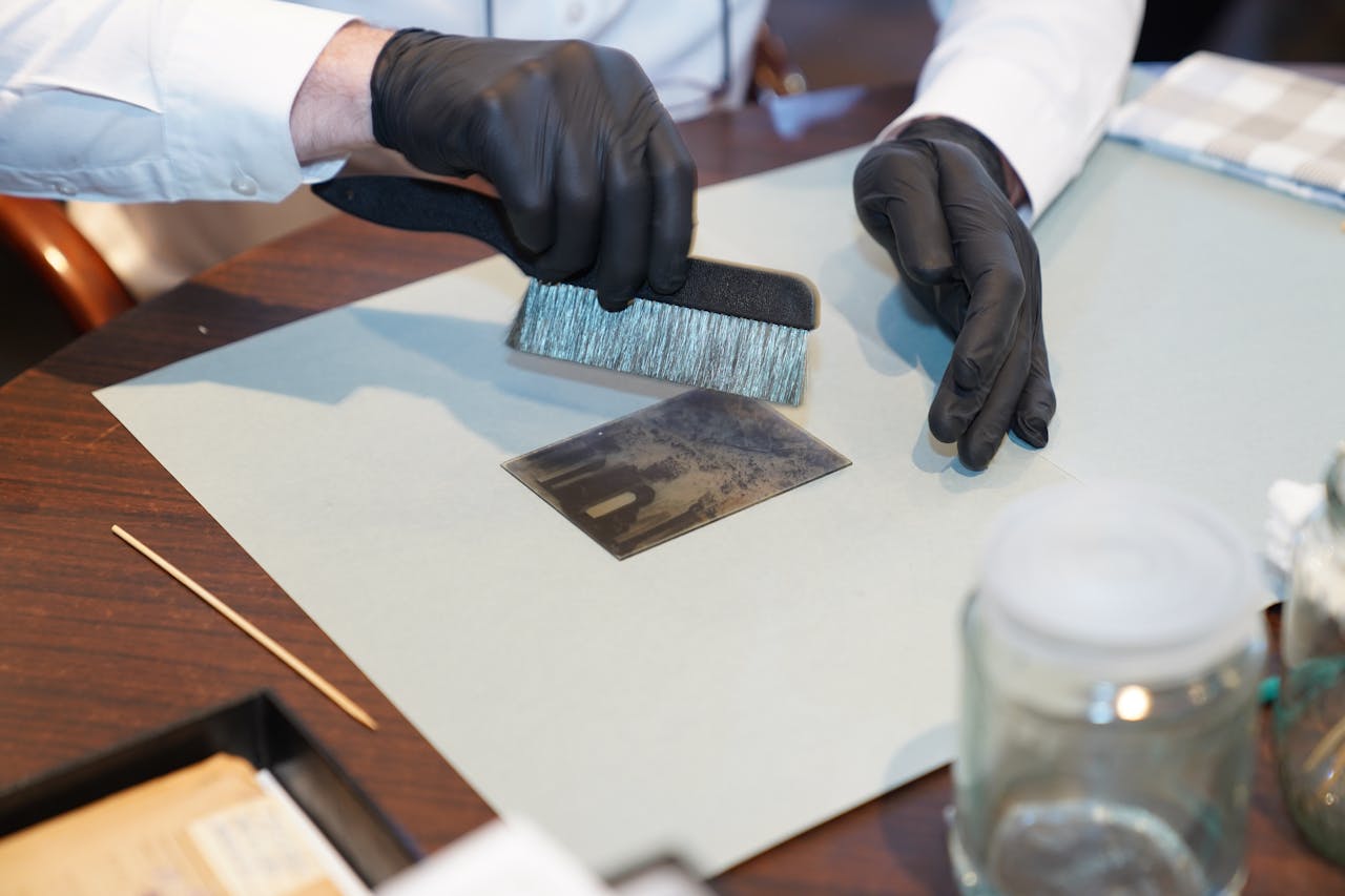 Close-up of photo preservation with a brush on a table, featuring black gloves.